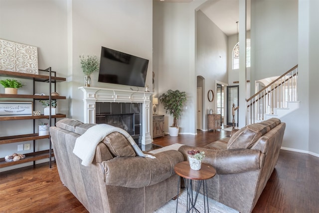 8508 Forsythia Dr, Mckinney, TX 75072 - living room featuring a high ceiling, arched walkways, wood finished floors, a tile fireplace, and stairs