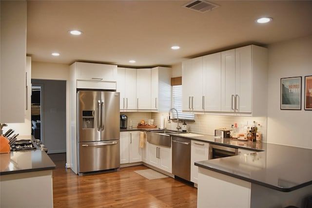 2542 Woodmere Dr, Dallas, TX 75233 - kitchen featuring stainless steel appliances, a peninsula, white cabinets, dark countertops, and recessed lighting