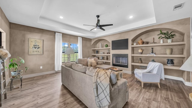 1381 County Road 1470, Chico, TX 76431 - living room with a raised ceiling, a fireplace, a ceiling fan, built in features, and light wood-style floors