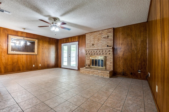 328 Bennett Cir, Desoto, TX 75115 - unfurnished living room with wood walls, ceiling fan, a textured ceiling, a fireplace, and french doors