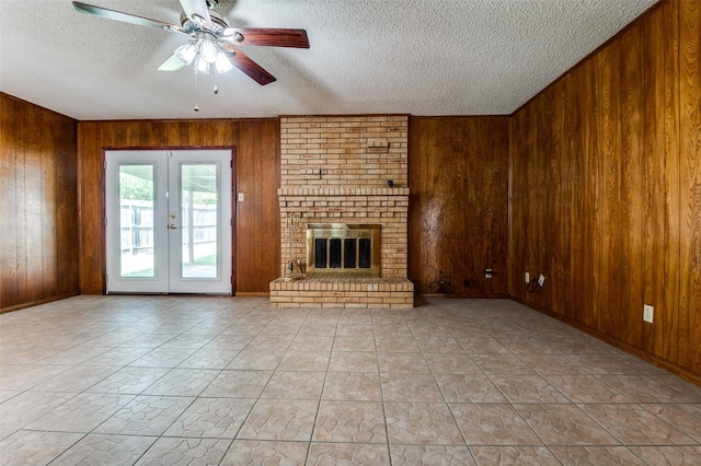 328 Bennett Cir, Desoto, TX 75115 - unfurnished living room featuring a textured ceiling, wood walls, a ceiling fan, french doors, and a fireplace