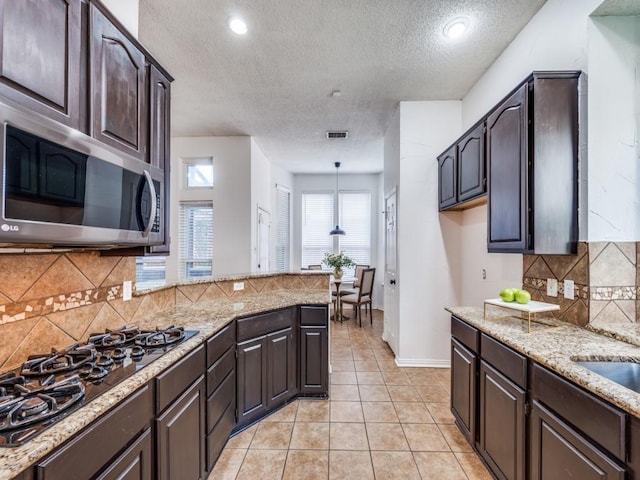1728 Forest Glen Dr, Flower Mound, TX 75028 - kitchen with stainless steel microwave, a textured ceiling, black gas cooktop, dark brown cabinets, and light stone countertops