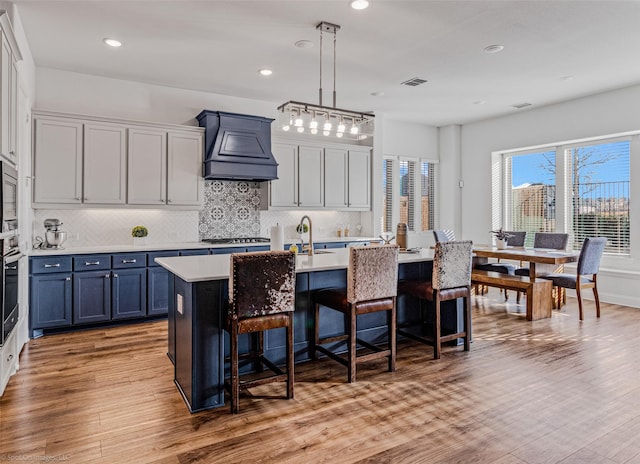 2010 Topaz Dr, Rockwall, TX 75087 - kitchen with custom exhaust hood, a breakfast bar area, light wood finished floors, light countertops, and recessed lighting