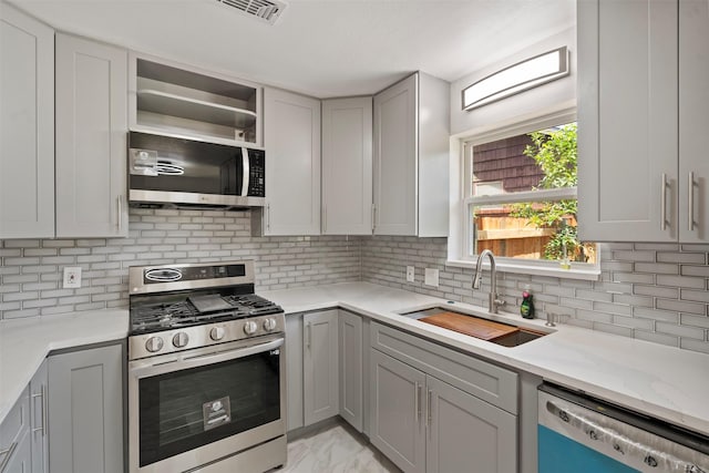 1228 Brookside Dr, Hurst, TX 76053 - kitchen with appliances with stainless steel finishes, gray cabinetry, light marble finish flooring, and tasteful backsplash