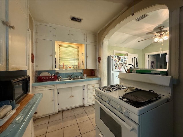 7032 Wofford Ave, Dallas, TX 75227 - kitchen featuring tile counters, white appliances, light tile patterned floors, white cabinets, and arched walkways