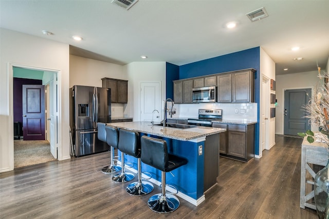 1315 Blessed Ln, Royse City, TX 75189 - kitchen featuring appliances with stainless steel finishes, a kitchen breakfast bar, light stone countertops, dark wood finished floors, and a center island with sink