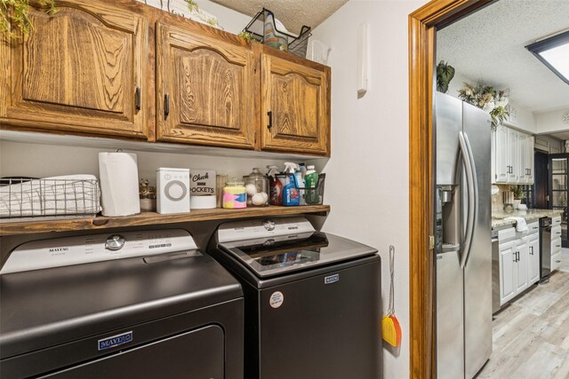 3244 Gail Ct, Irving, TX 75060 - laundry room featuring cabinet space, washer and clothes dryer, light wood-style floors, and a textured ceiling