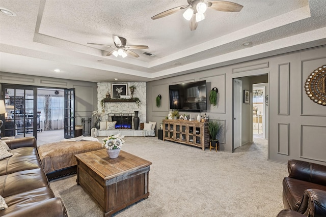 3244 Gail Ct, Irving, TX 75060 - carpeted living area featuring ceiling fan, a textured ceiling, a tray ceiling, and a stone fireplace