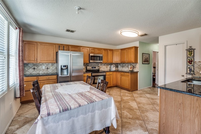 2007 Brazos Ct, Grand Prairie, TX 75052 - kitchen with stainless steel appliances, decorative backsplash, a textured ceiling, brown cabinetry, and dark stone countertops