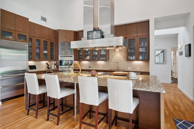 613 N Bailey Ave, Fort Worth, TX 76107 - kitchen featuring stainless steel appliances, backsplash, a high ceiling, light wood finished floors, and glass insert cabinets