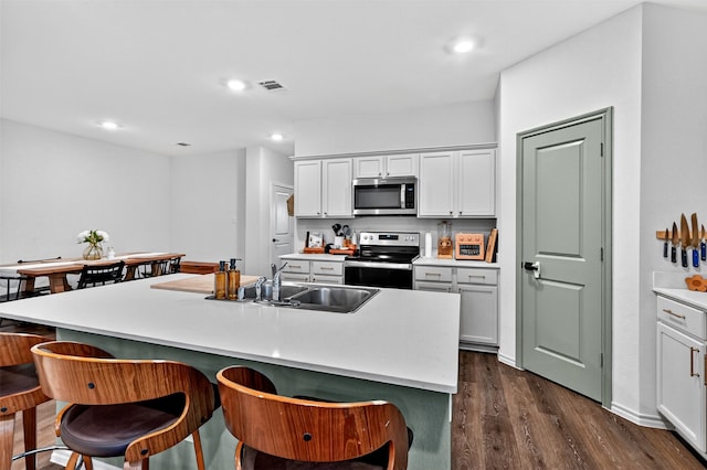 2806 Peony Dr, Sherman, TX 75092 - kitchen with stainless steel appliances, a kitchen bar, dark wood-style flooring, recessed lighting, and white cabinetry