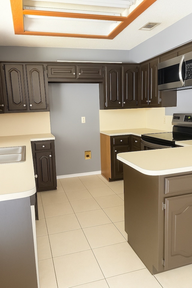 202 Modene Ave, Waxahachie, TX 75165 - kitchen with stainless steel appliances, light countertops, light tile patterned floors, and dark brown cabinets