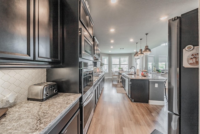 407 Emerson Dr, Rockwall, TX 75087 - kitchen featuring appliances with stainless steel finishes, light wood-type flooring, recessed lighting, light stone countertops, and an island with sink