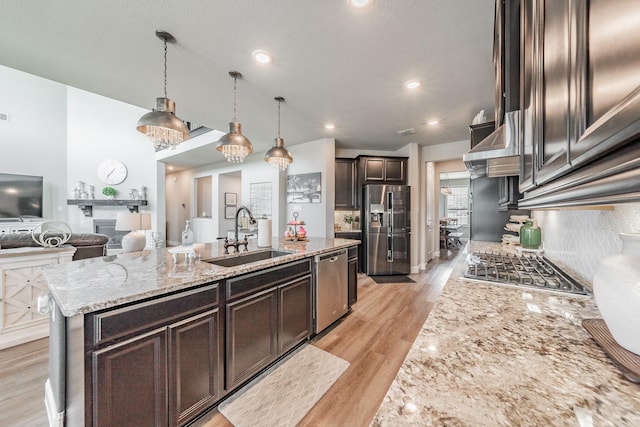 407 Emerson Dr, Rockwall, TX 75087 - kitchen with stainless steel appliances, dark brown cabinets, a center island with sink, light stone countertops, and light wood-type flooring
