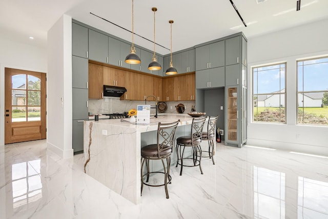 1022 Bow St, Rockwall, TX 75087 - kitchen with light marble finish floors, under cabinet range hood, decorative backsplash, light stone countertops, and decorative light fixtures