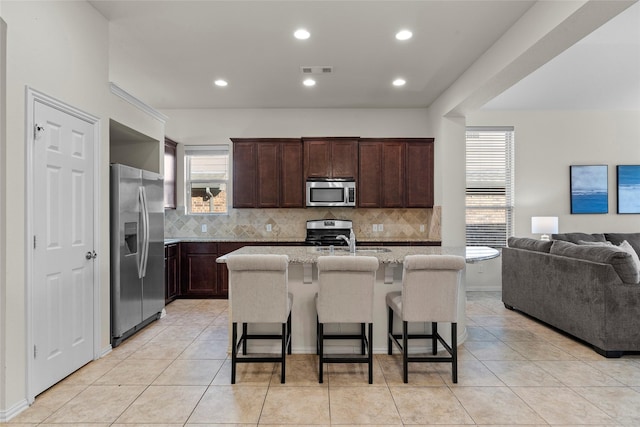 5201 Datewood Ln, Mckinney, TX 75071 - kitchen with stainless steel appliances, open floor plan, tasteful backsplash, dark brown cabinets, and a kitchen bar