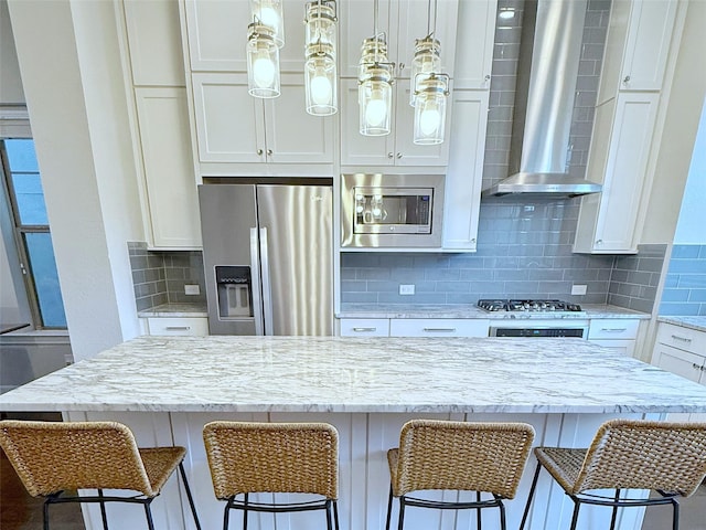 5339 Holland Ave, Dallas, TX 75209 - kitchen featuring stainless steel appliances, wall chimney range hood, white cabinetry, decorative backsplash, and a breakfast bar area