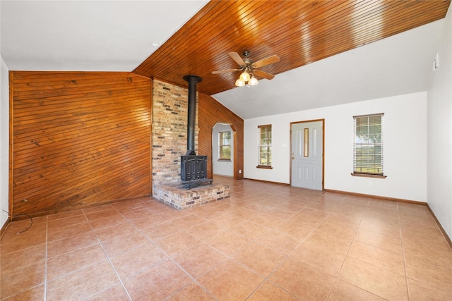 10900 Fm 1189, Lipan, TX 76462 - unfurnished living room with lofted ceiling, a wood stove, wood walls, a ceiling fan, and healthy amount of natural light