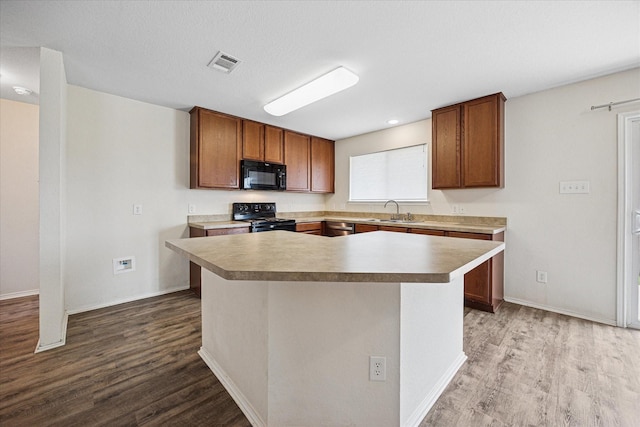 330 Broken Bow, Krum, TX 76249 - kitchen featuring black appliances, wood finished floors, light countertops, brown cabinetry, and a center island