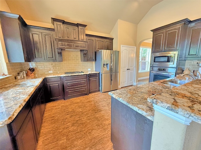 14249 Fall Harvest Dr, Frisco, TX 75033 - kitchen featuring stainless steel appliances, lofted ceiling, dark brown cabinetry, arched walkways, and backsplash