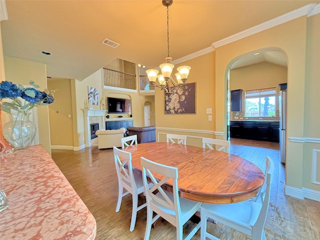 14249 Fall Harvest Dr, Frisco, TX 75033 - dining space featuring arched walkways, a fireplace, a chandelier, wood finished floors, and ornamental molding