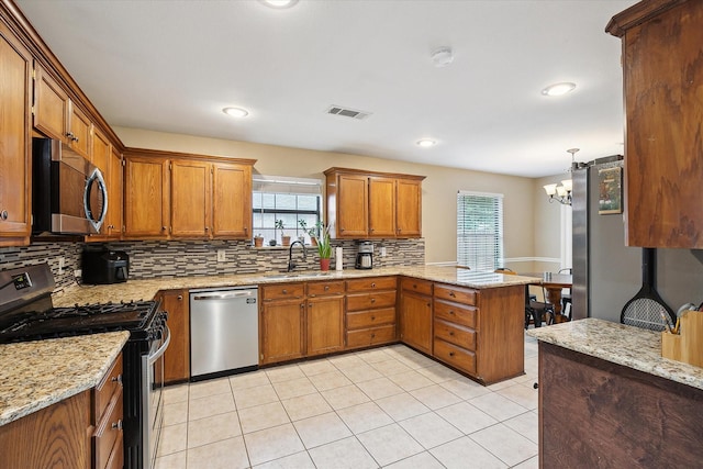 1112 Indian Ridge Dr, Denton, TX 76205 - kitchen featuring appliances with stainless steel finishes, a peninsula, backsplash, brown cabinetry, and plenty of natural light