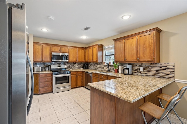 1112 Indian Ridge Dr, Denton, TX 76205 - kitchen featuring appliances with stainless steel finishes, a peninsula, brown cabinets, backsplash, and light tile patterned floors