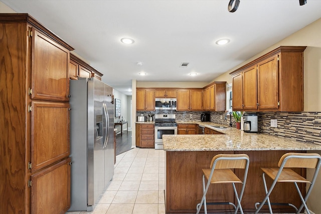1112 Indian Ridge Dr, Denton, TX 76205 - kitchen with stainless steel appliances, a peninsula, brown cabinetry, decorative backsplash, and light tile patterned floors