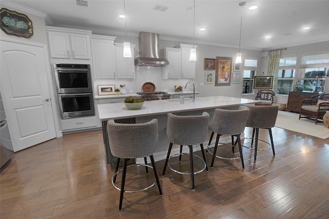 717 Freedom Ln, Aubrey, TX 76227 - kitchen featuring wall chimney exhaust hood, stainless steel double oven, crown molding, light countertops, and a kitchen bar