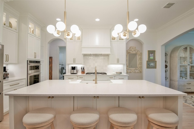 1001 Quarry Ct, Granbury, TX 76048 - kitchen with appliances with stainless steel finishes, a chandelier, custom range hood, arched walkways, and crown molding