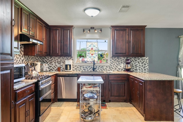 845 Griffith Ave, Terrell, TX 75160 - kitchen with stainless steel appliances, under cabinet range hood, a peninsula, decorative backsplash, and light stone countertops