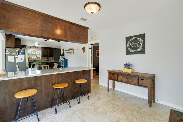 845 Griffith Ave, Terrell, TX 75160 - kitchen with freestanding refrigerator, light stone countertops, a breakfast bar, decorative backsplash, and dark brown cabinetry