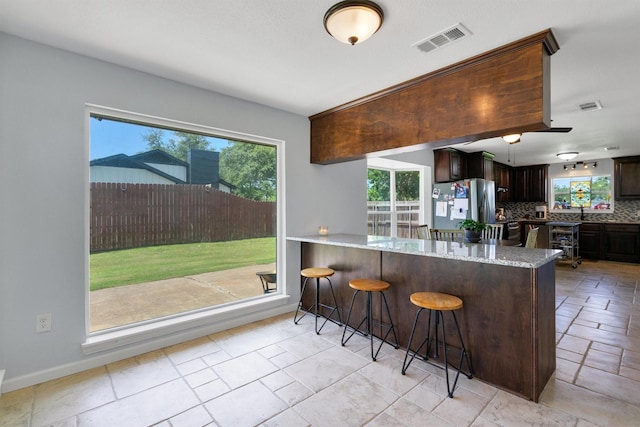 845 Griffith Ave, Terrell, TX 75160 - kitchen with stainless steel refrigerator with ice dispenser, dark brown cabinets, light stone counters, backsplash, and a peninsula