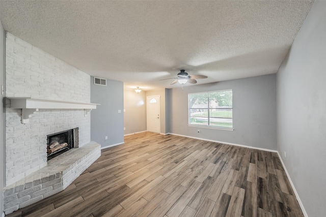 5105 French Wood Dr, Arlington, TX 76016 - unfurnished living room featuring wood finished floors, ceiling fan, a brick fireplace, and a textured ceiling