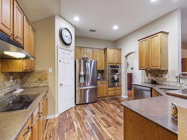 1597 Sweetbriar Dr, Allen, TX 75002 - kitchen with appliances with stainless steel finishes, wood finished floors, arched walkways, recessed lighting, and dark stone countertops