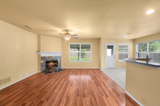 108 Bear Trl, Waxahachie, TX 75165 - unfurnished living room featuring light wood-style flooring, a tile fireplace, ceiling fan, and healthy amount of natural light