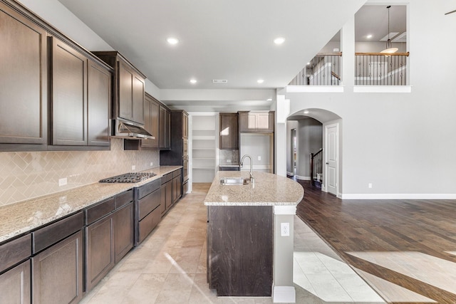 1800 Trotter Trl, Aubrey, TX 76227 - kitchen featuring arched walkways, light stone countertops, a center island with sink, dark brown cabinetry, and recessed lighting