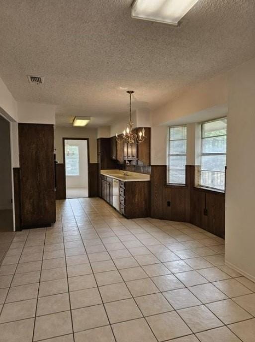 1601 Meadow Ln, Terrace, Fort Worth, TX 76112 - kitchen featuring a textured ceiling, a chandelier, wood walls, light countertops, and dark brown cabinets