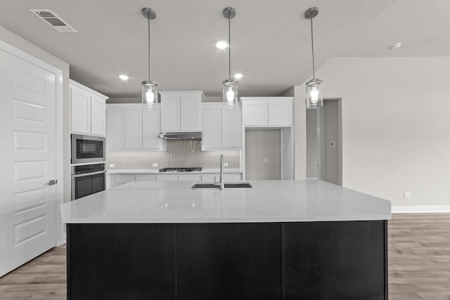6217 Escarpment Dr, Fort Worth, TX 76112 - kitchen with stainless steel appliances, light wood-style flooring, tasteful backsplash, a spacious island, and white cabinetry