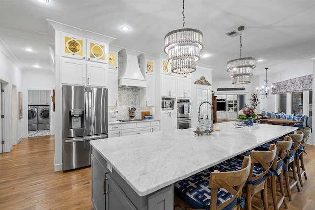 7116 Serrano Dr, Benbrook, TX 76126 - kitchen featuring stainless steel appliances, independent washer and dryer, premium range hood, a chandelier, and white cabinets