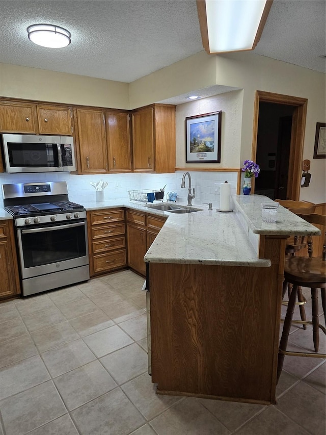 3810 Lucena Ct, Grand Prairie, TX 75052 - kitchen featuring appliances with stainless steel finishes, a peninsula, brown cabinetry, a textured ceiling, and a kitchen breakfast bar