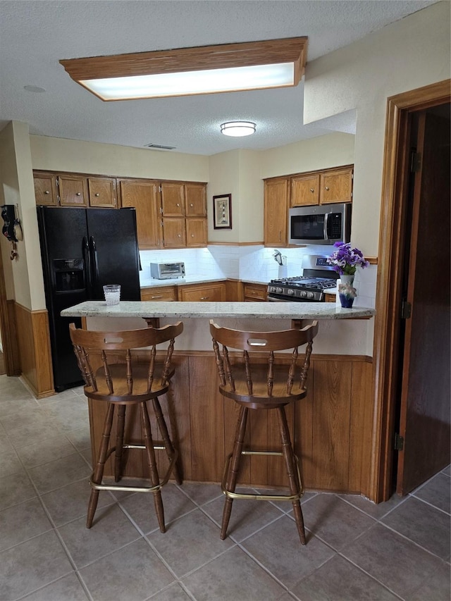 3810 Lucena Ct, Grand Prairie, TX 75052 - kitchen featuring appliances with stainless steel finishes, brown cabinetry, a peninsula, light countertops, and tile patterned flooring