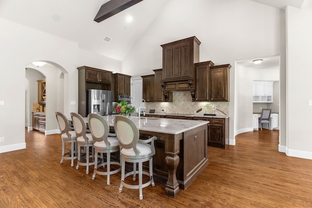 1707 Ponderosa Trl, Sachse, TX 75048 - kitchen with high vaulted ceiling, stainless steel refrigerator with ice dispenser, a kitchen island with sink, dark brown cabinets, and wood finished floors