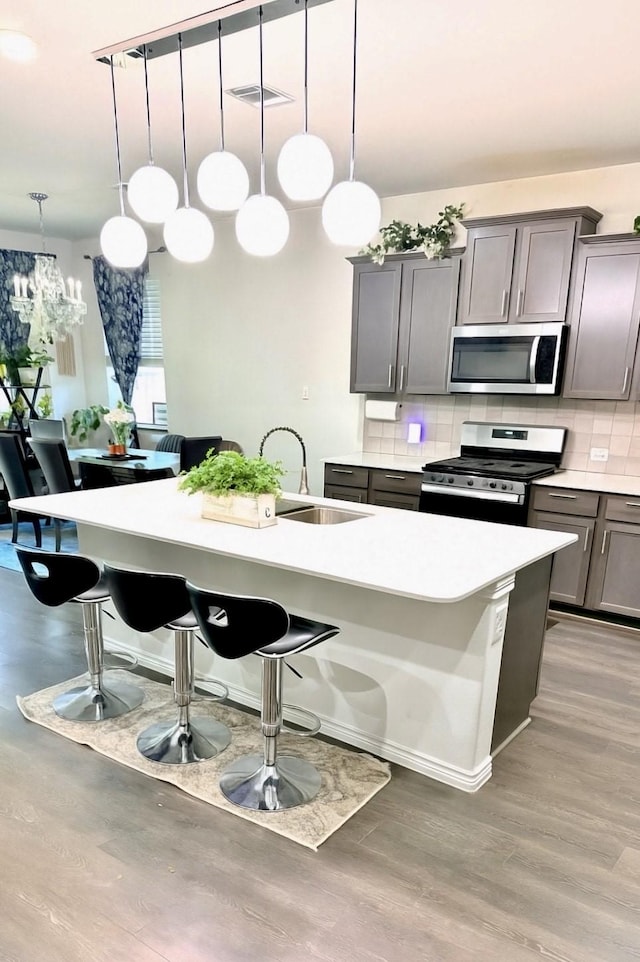 3316 Azure Ln, Celina, TX 75009 - kitchen with appliances with stainless steel finishes, gray cabinets, a kitchen bar, tasteful backsplash, and light wood-type flooring