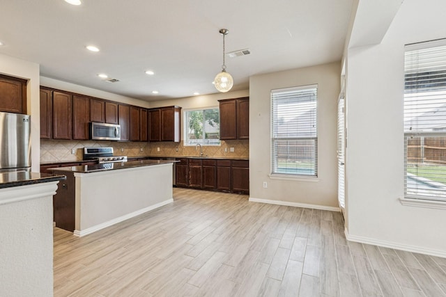 326 Blackhaw Dr, Fate, TX 75087 - kitchen with appliances with stainless steel finishes, decorative backsplash, light wood finished floors, dark brown cabinetry, and hanging light fixtures