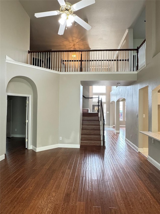 4712 Englishtown Dr, Arlington, TX 76016 - unfurnished living room with arched walkways, hardwood / wood-style flooring, a ceiling fan, stairway, and a high ceiling