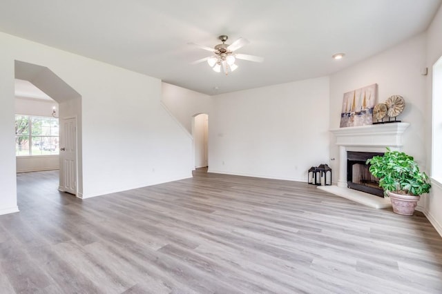 2601 Pinto Dr, Denton, TX 76210 - unfurnished living room with arched walkways, ceiling fan, a fireplace with raised hearth, and light wood-style floors
