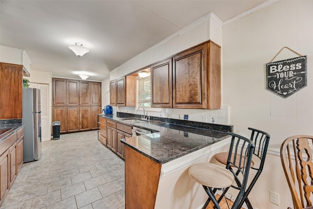 1719 W Day St, Denison, TX 75020 - kitchen featuring freestanding refrigerator, a peninsula, a kitchen breakfast bar, brown cabinets, and dark stone counters