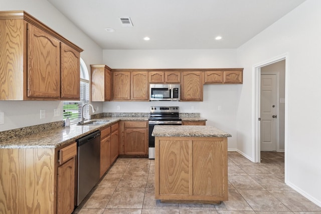 5901 Ozark Dr, Fort Worth, TX 76131 - kitchen with stainless steel appliances, a center island, light stone countertops, brown cabinets, and recessed lighting