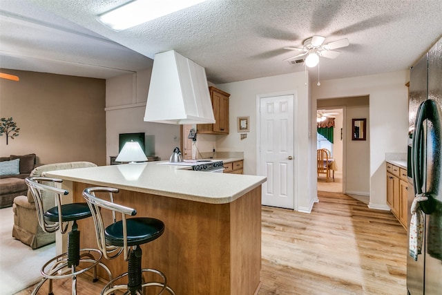 5312 Vermillion Trl, Arlington, TX 76017 - kitchen with premium range hood, a ceiling fan, black fridge, a breakfast bar, and a textured ceiling